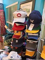 Rack of assorted sports caps showing multiple team logos and colors in a room.