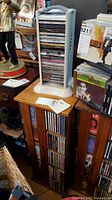 White plastic CD holder containing vertically stacked music CDs of various genres, placed on a wooden surface alongside other music collections.