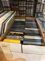 Box with multiple DVDs stacked inside, visible black cases with some artist covers partially visible.