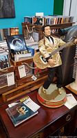 Full view of Elvis Presley statue standing on a circular base, holding a guitar, surrounded by CDs and other items.
