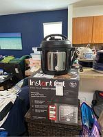Front view of Instant Pot Pro Plus multi-cooker on original box with kitchen background.