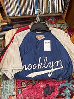 Stack of jerseys front, showing navy Brooklyn Dodgers script jersey on top