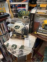 Overall view of signed helmet in display case with T-shirt draped below and Namath book beside