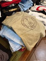 Stack of folded T-shirts, highlight light gray Life is Good shirt with guitar logo on top