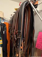 Side view showing multiple men's belts hanging, mostly leather with various metal buckle styles and colors.