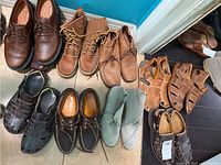 Top view photo showing all 10 pairs of shoes arranged on a floor, varying styles and colors including brown leather, tan boots, and dark woven sandals.