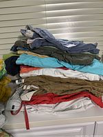 Stack of men's shorts in various colors including blue, khaki, red, white, and green with folded pants and some drawstrings visible