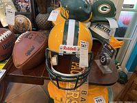 Photo showing Green Bay Packers Riddell decorative helmet, two footballs, and hats arranged on a table.