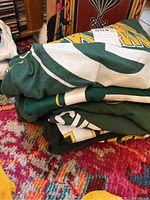 Stack of folded Green Bay Packers T-shirts showing green fabric with white and yellow graphics.