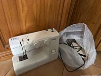 Full side view of Simplicity sewing machine with foot pedal in plastic bag placed beside it on floor