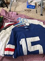 Blue sweatshirt with number 15 and sleeve stripes visible on hangers over other jerseys
