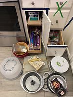 Overview of the baking pans, cake carriers, wraps, and mixing bowls in front of cabinets and drawers, showing most items in the lot.