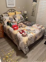 Full bed with metal frame, quilted patchwork bedspread, four pillows, and miscellaneous excluded items on top.