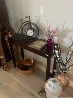Wide angle photo showing the console table with the bicycle clock, framed picture, and mason jar vase on top, along with other decorative items nearby.