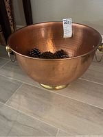 Wide angle shot showing the copper wash bin including interior and side handles, positioned on floor with pine cones inside.