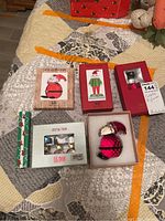 Five boxed crystal Christmas figurines and a black pen arranged on a patterned quilted surface. Boxes feature festive designs and windows showing the figurines inside.