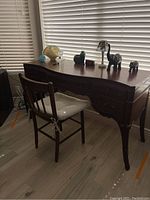 Side view of vintage wooden desk and chair set near window with decorative items on desk surface.