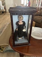 Full view of BK Collectibles doll in ornate wooden and glass display case on wooden table.