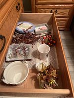 Partial view inside dresser drawer with white ceramic bowl, white coffee cup, seasonal dish and stemmed floral berries.