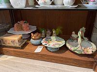 Fitz and Floyd Garden Rhapsody spring themed set on wooden shelf including serving dish, cake platter, faux cake, ceramic bunny dish, duck figurines, and floral candle.