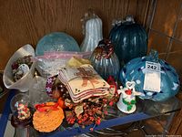Wide view of various holiday decor items including glass gourds, miniature wreaths, faux fall cupcake, assorted jewelry and sachets