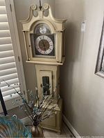 Full view of floor clock showing wooden case, arched hood, two glass doors and pendulum