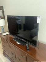 Full front angled view of the 40 inch TCL HDTV sitting on wood dresser with remote in front.