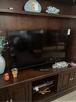 Front view of the 50-inch Insignia HDTV on a wooden cabinet with remote placed in front and decorative candles beside.