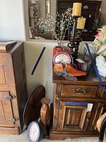 Photo showing bicycle-shaped table clock, wooden candle stick holders with candles, decorative shoes, glass vase with faux plant, faux orange vase, and decorative plate in background.