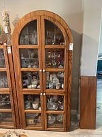 Front view of oak wood curved-top hutch with glass pane doors containing display items inside.