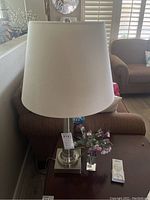 Aluminum base lamp with white shade on side table near couch.
