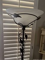 Full view of the top bowl-shaped frosted glass shade held by black metal vine accented frame