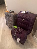 Three pieces of luggage on floor including a camouflage upright bag, a large burgundy suitcase, and a smaller carry-on burgundy bag.