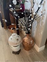 Photo showing the copper-tone metal vase with faux decorative branches and the white and pink floral vintage lamp beside a mirror and floor molding.