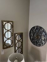Three rectangular wall mirrors each with three overlapping circular mirrors framed in distressed wood, shown on a wall corner with lamp below.