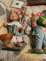 Photo showing three different stuffed rabbit dolls lying on quilted surface with basket and carrot accessories.