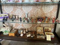 Display shelf with rows of various small ceramic and porcelain shoe figurines, some with small boxes underneath, a ceramic bird statue, and small decorative items.