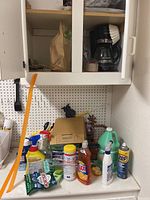 Image of various household cleaning bottles, coffee pot in cabinet, and cleaning accessories on shelf and countertop.