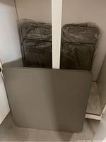 Two stacks of four folding chairs wrapped in plastic stored behind a grey folding table.