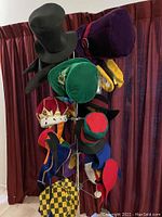 Multiple whimsical hats arranged on a metal hat stand against dark curtain background
