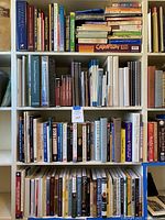 Four bookshelf units each filled with a variety of books focused on investing, self-help, personal development, and money management topics. Books vary in size, color and type from hardback to paperback.