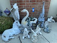 Multiple resin garden statues including elephant fountain, swan, horse, fairy figures, and woman playing harp arranged against a brick wall showing size and condition.