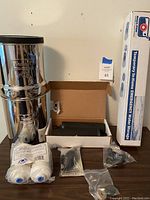 Full setup on tabletop showing stainless steel tower, filter elements, PF-2 cartridges, primer pump and AquaPod box