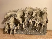 Front view of the full sculpture showing five horses jumping forward from stylized ocean waves with detailed facial features and flowing manes in gray finish.