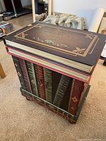 Multi-colored wooden side table with a rectangular top resembling book covers and spines, shown on carpeted floor near furniture and decor.