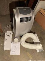 Front view of the Edgestar AP12001S portable air conditioner with vent hose, window mounting plate, and user manual laid out on the floor.