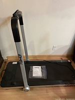 Full view of the treadmill with foldable handrail standing upright on a wooden floor.