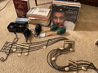 Overview of large lot showing a stack of piano sheet music, encyclopedia book, maracas, microphones, and musical note wall art on carpeted floor.