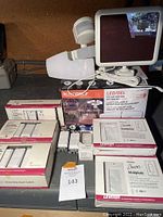 Photo of various Leviton Decora white wall plates, light switches, outlets, and a Sunforce solar motion light with labels and boxes visible.