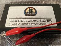 Black rectangular colloidal silver generator labeled 2020 Classic Generator Model 2.4 with red alligator clips on bubble wrap.